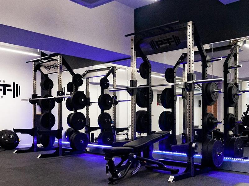 Twin power racks with loaded barbells and an adjustable bench, purple accent lighting