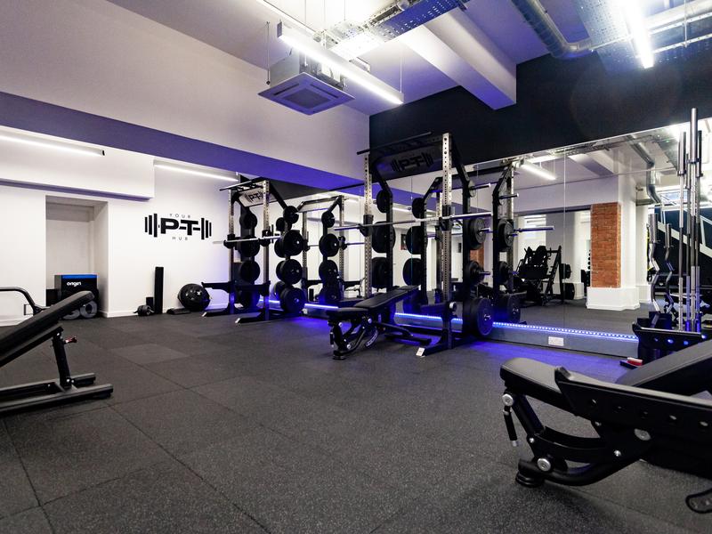 Power rack and free-weight station at Your PT Hub's Islington studio, with the studio's wall logo and mirrored wall behind